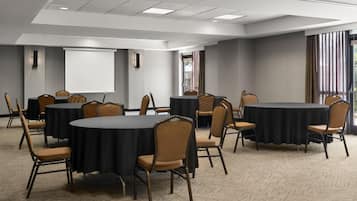 Un salón de conferencias con mesas redondas, sillas, una pantalla de proyector y suelo alfombrado.