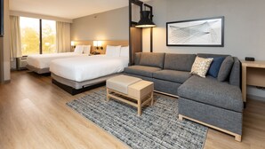 A hotel room with two beds, a sofa, a coffee table, and a large window with curtains.