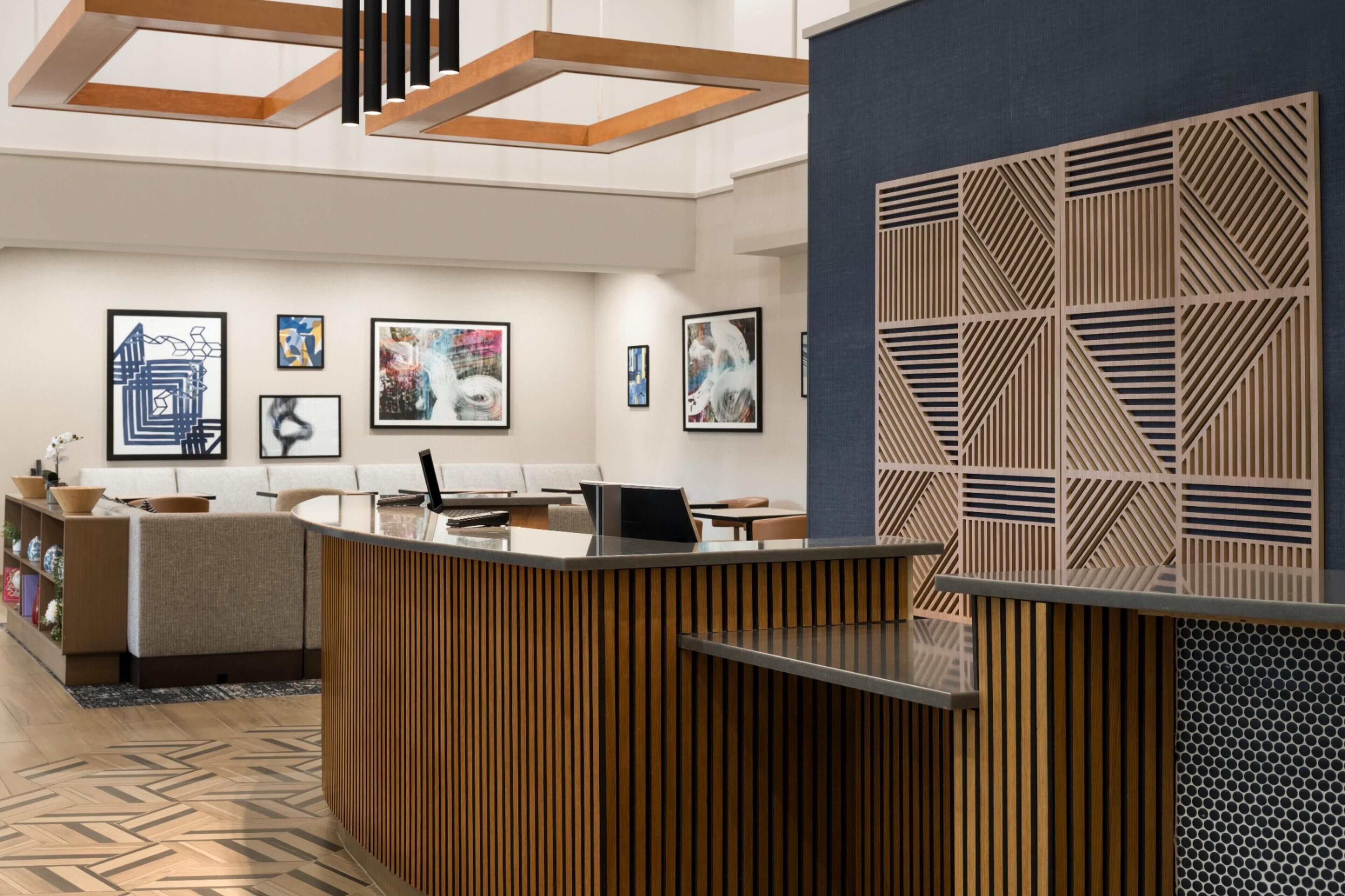 Un área de recepción moderna con un mostrador de madera, un espacio de descanso con sofá y una pared decorada con arte abstracto.