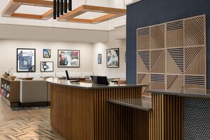 A modern reception area with a wooden reception desk, a seating area with a sofa, and a wall with abstract art. - Hyatt Place Dallas/Park Central (Dallas)