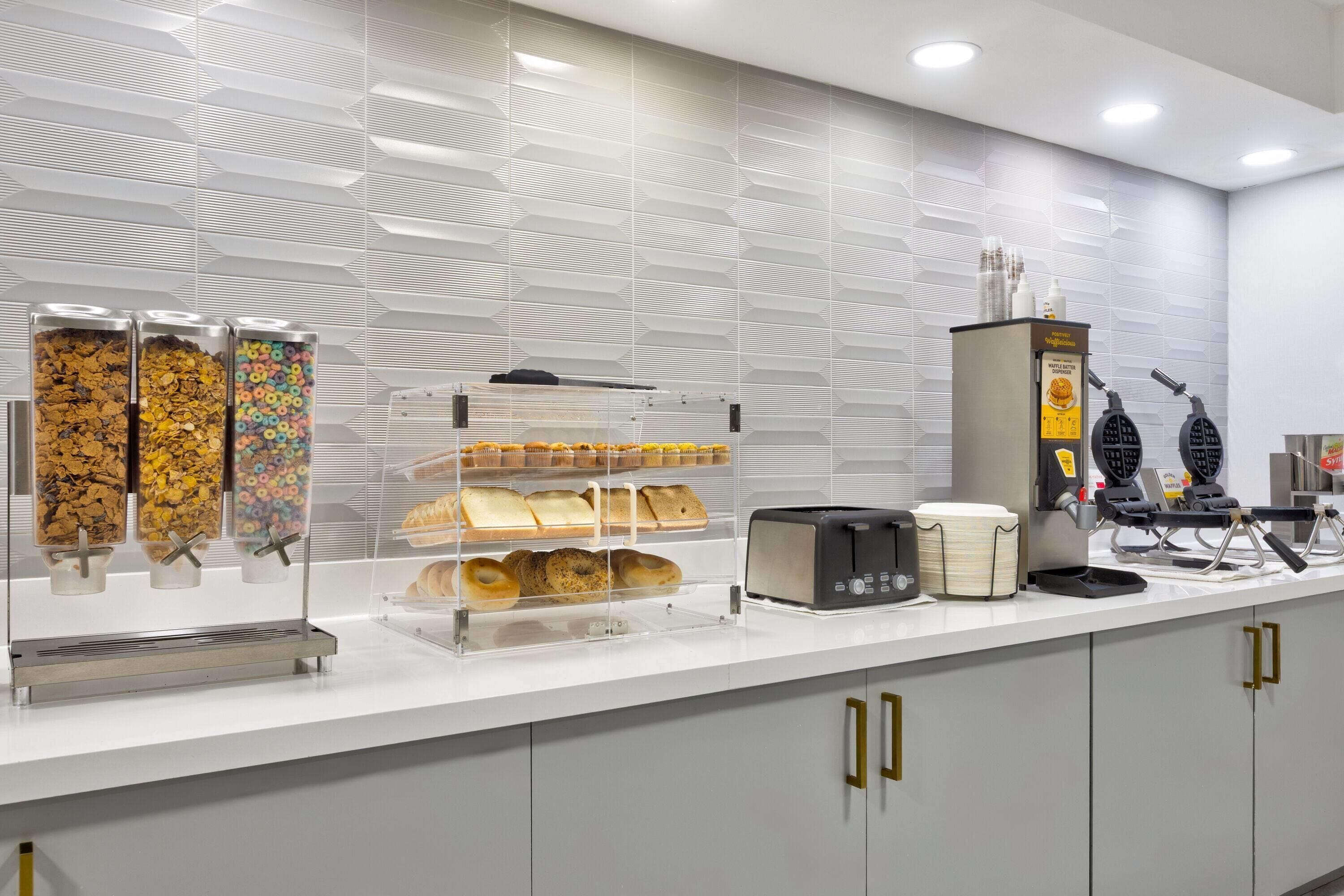 A breakfast bar with cereal, bagels, and a coffee machine.