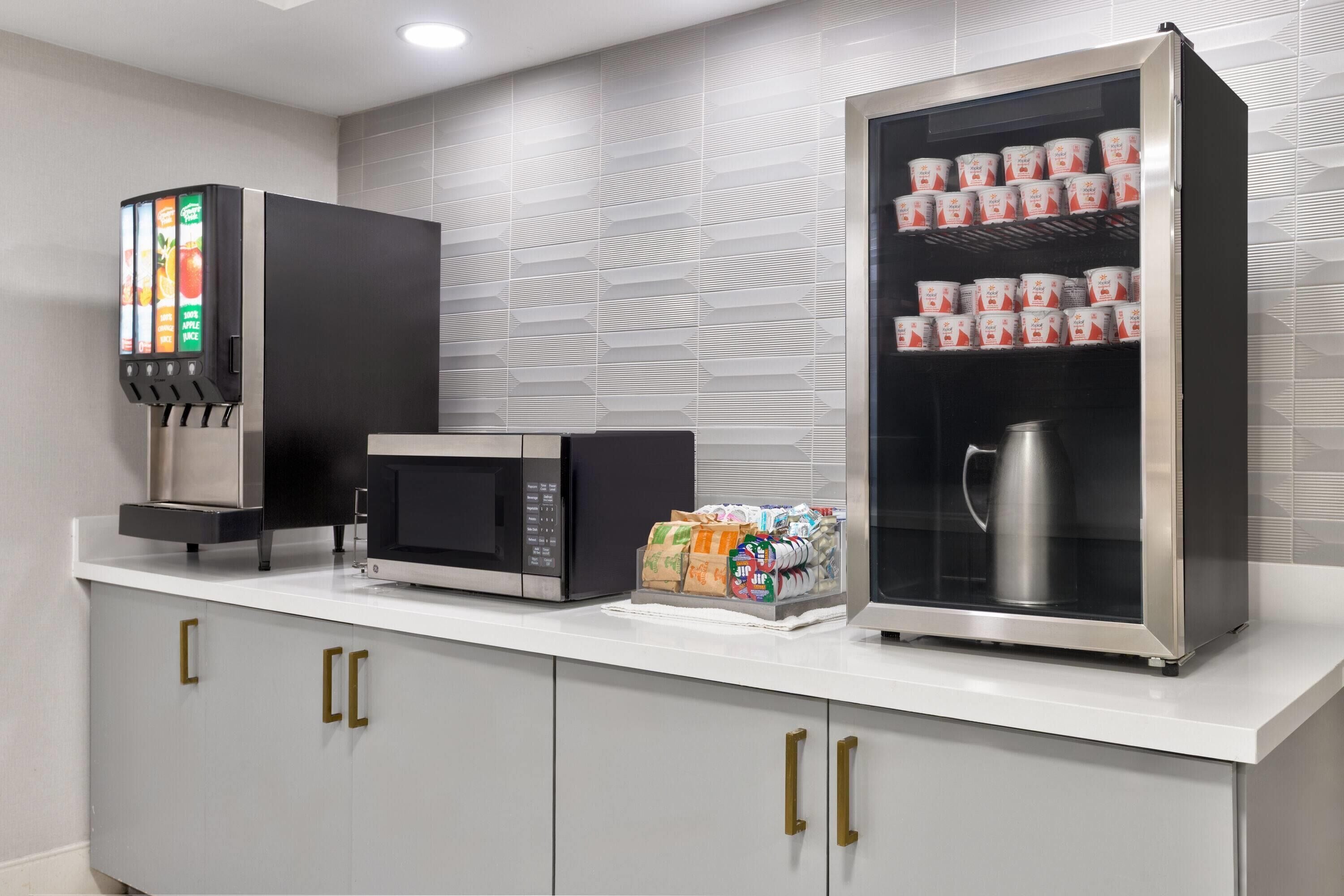 A kitchenette with a coffee machine, microwave, and refrigerated display case.