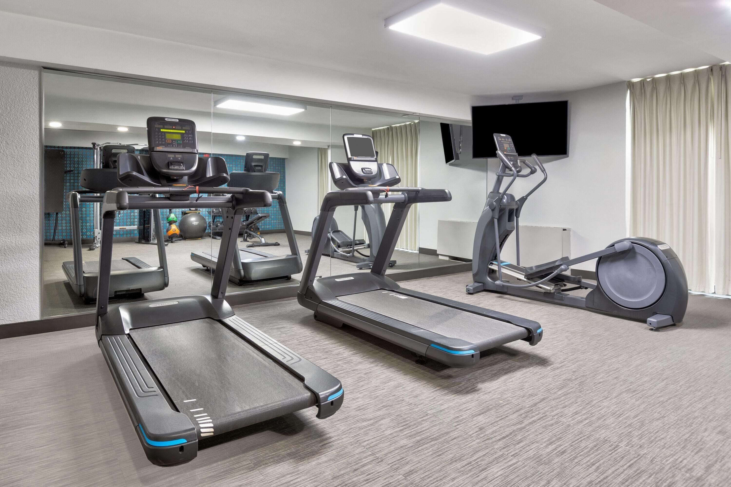 Ein Fitnessstudio mit Laufbändern, Crosstrainern und einem stationären Fahrrad.