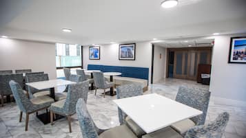 Un espace repas moderne avec des chaises à revêtement bleu et des tables blanches, agrémenté d’un banc rembourré bleu et de tableaux encadrés aux murs.
