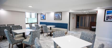 Un espace repas moderne avec des chaises à revêtement bleu et des tables blanches, agrémenté d’un banc rembourré bleu et de tableaux encadrés aux murs.