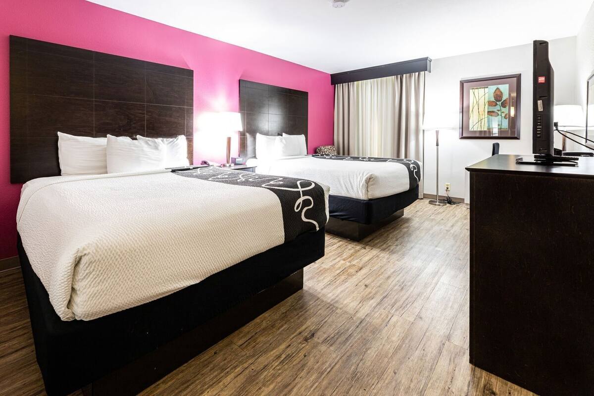 Een hotelkamer met twee bedden, een bureau, een stoel, een lamp en een schilderij aan de muur.
