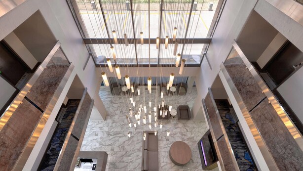 A modern hotel lobby with a high ceiling, marble flooring, a central seating area, and a large window providing natural light. - La Quinta Inn & Suites by Wyndham Dallas I-35 Walnut Hill Ln (Dallas)