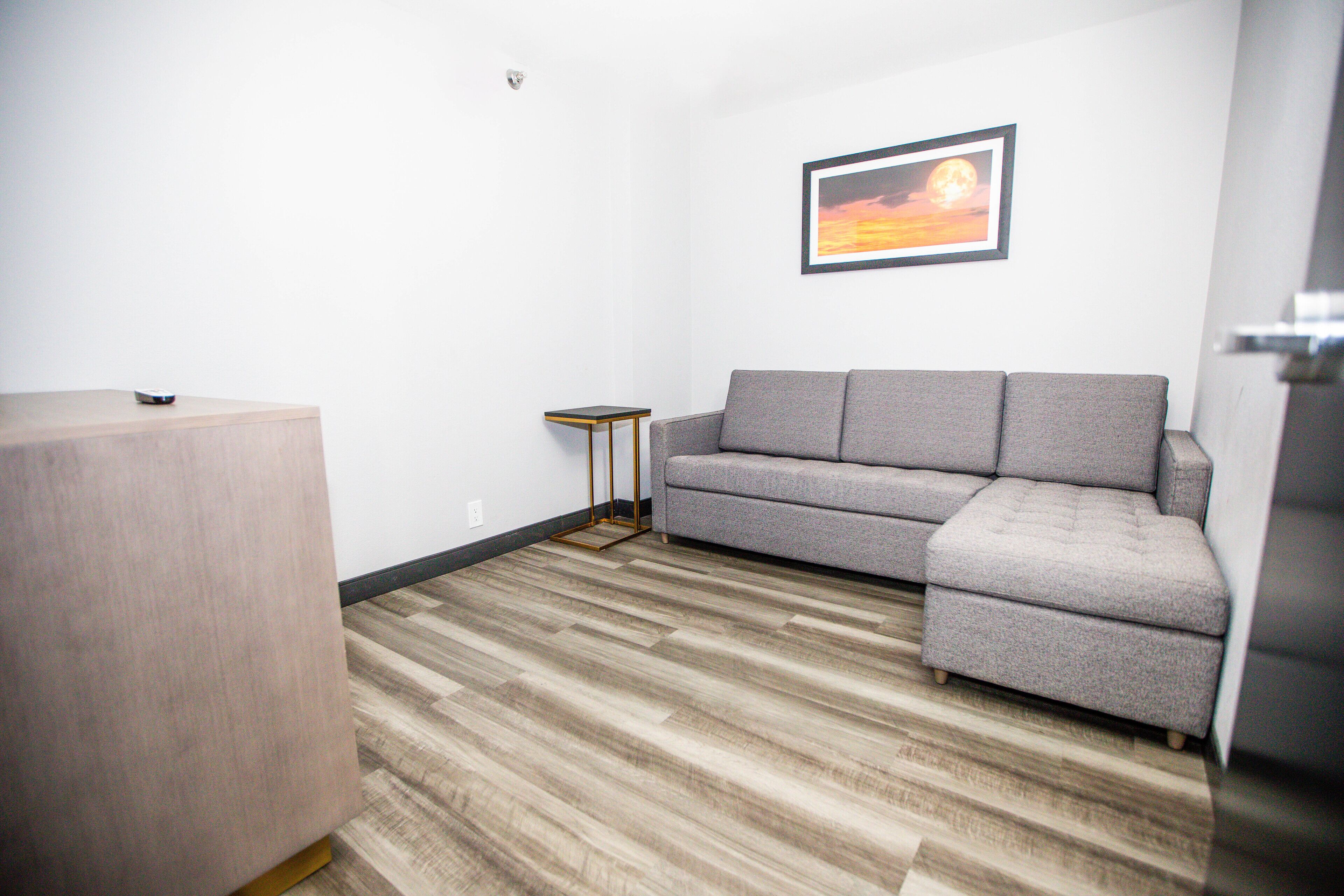 A modern living room with a grey sectional sofa, a small side table, and a wooden floor.
