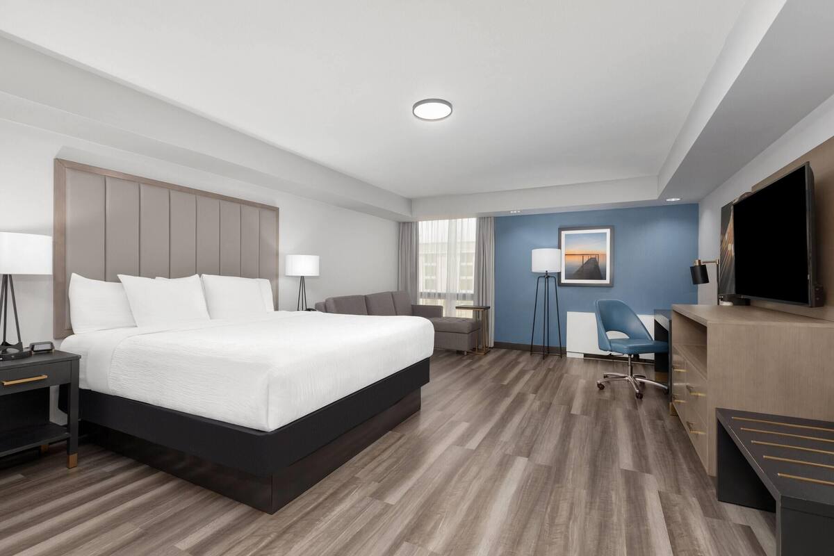 Een hotelkamer met een groot bed, nachtkastjes, een bureau met stoel, een televisie en een raam met gordijnen.
