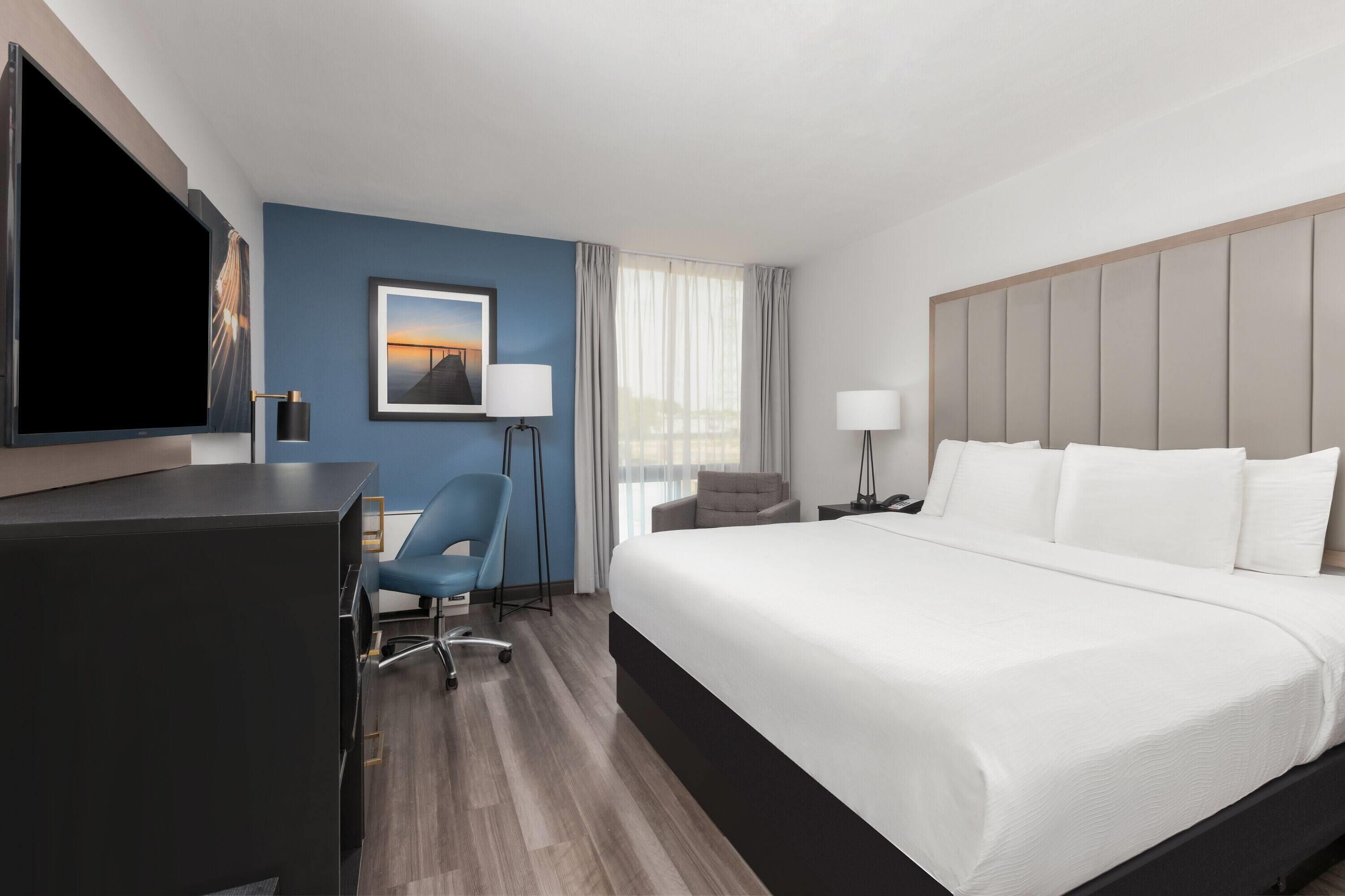 A hotel room with a bed, a desk, a chair, a TV, and a window with curtains.