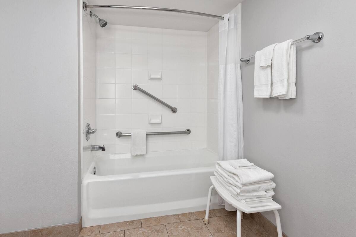 Een badkamer met een bad, een douche, een handgreep, een handdoekhouder en een stapel handdoeken.