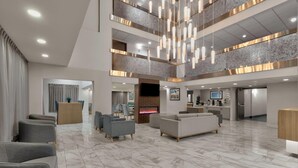 A spacious lobby with a high ceiling, modern lighting fixtures, a fireplace, and seating areas. - La Quinta Inn & Suites by Wyndham Dallas I-35 Walnut Hill Ln (Dallas)