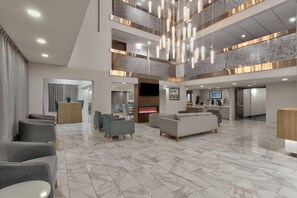 Un hall d’entrée spacieux avec un plafond haut, des luminaires modernes, une cheminée et des coins salon.