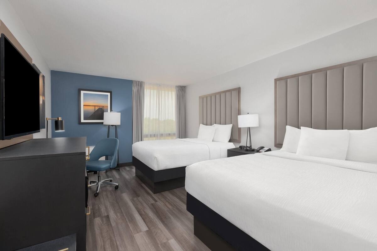 Hotelkamer met twee bedden, een bureau, een stoel, een televisie en een raam met gordijnen.