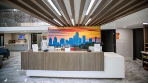 A modern reception desk with a city skyline mural, a marble floor, and a high ceiling with wooden beams. - La Quinta Inn & Suites by Wyndham Dallas I-35 Walnut Hill Ln (Dallas)
