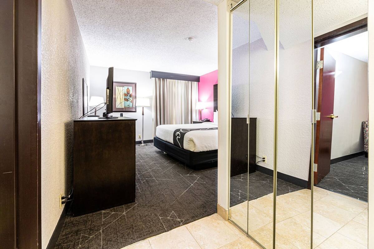 Een hotelkamer met een bed, bureau, lamp en een schilderij aan de muur.
