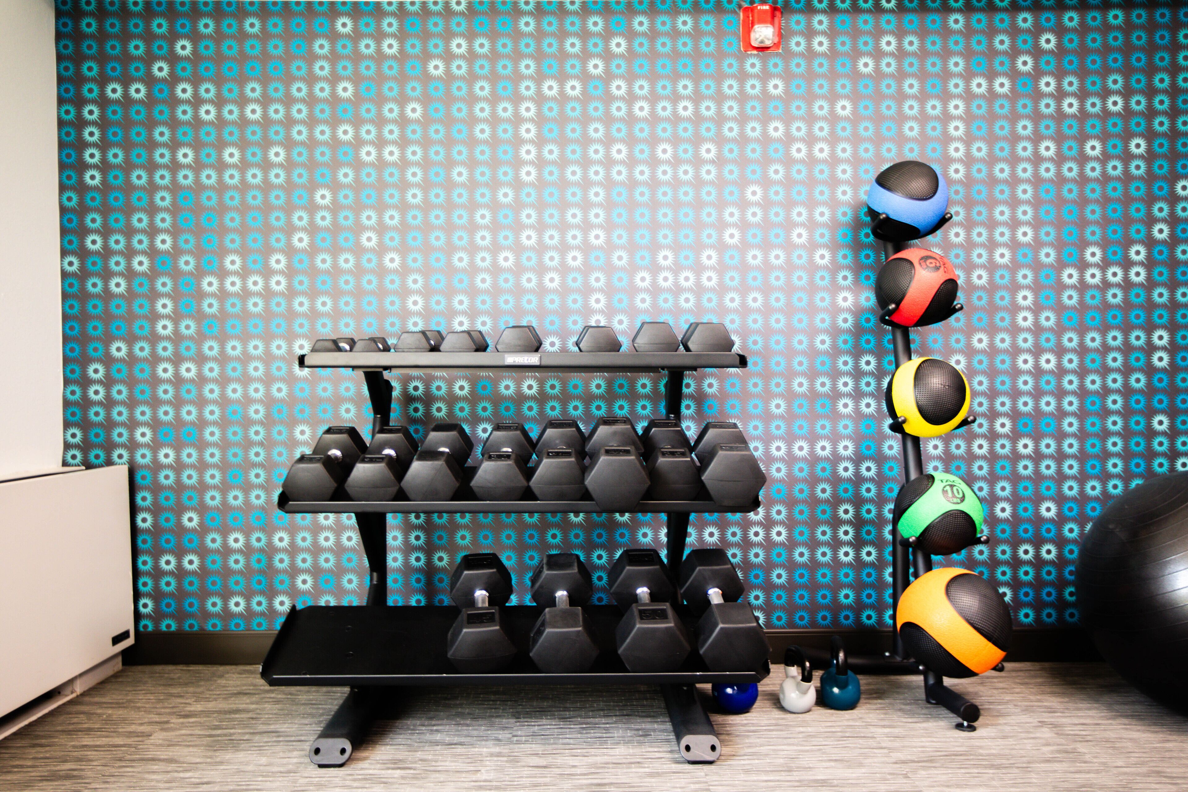 Ein Fitnessraum mit Wandpaneelen mit Muster, einer Hantelbank, Kettlebells und Trainingsbällen.