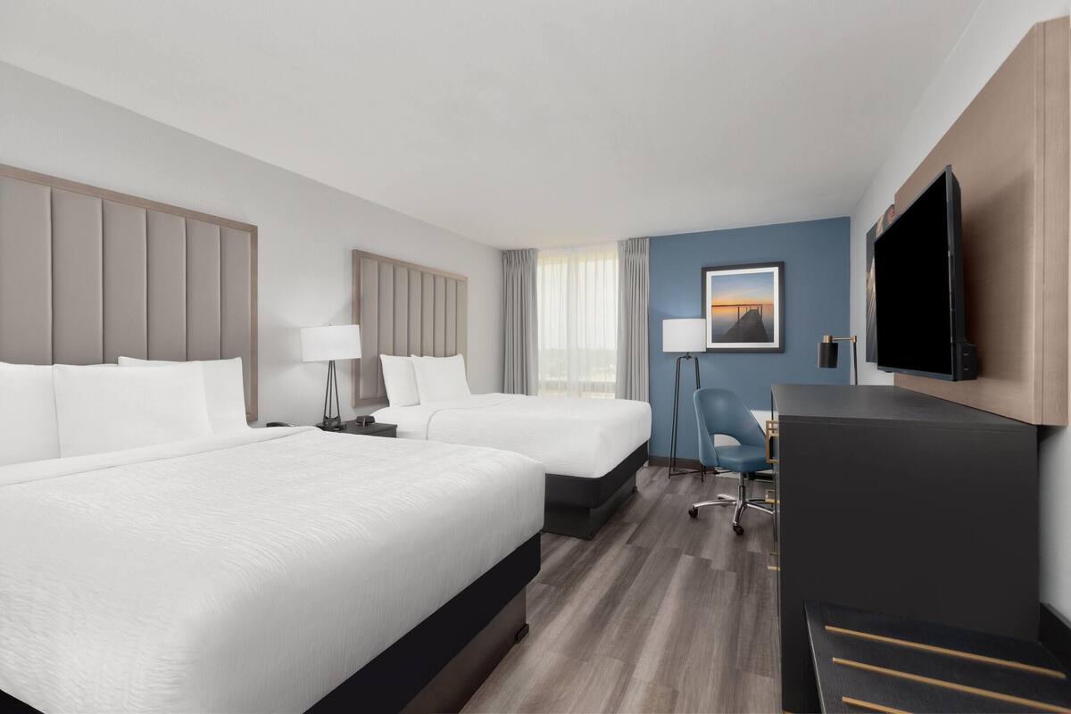 Een hotelkamer met twee bedden, een bureau, een stoel, een televisie en een raam met gordijnen.