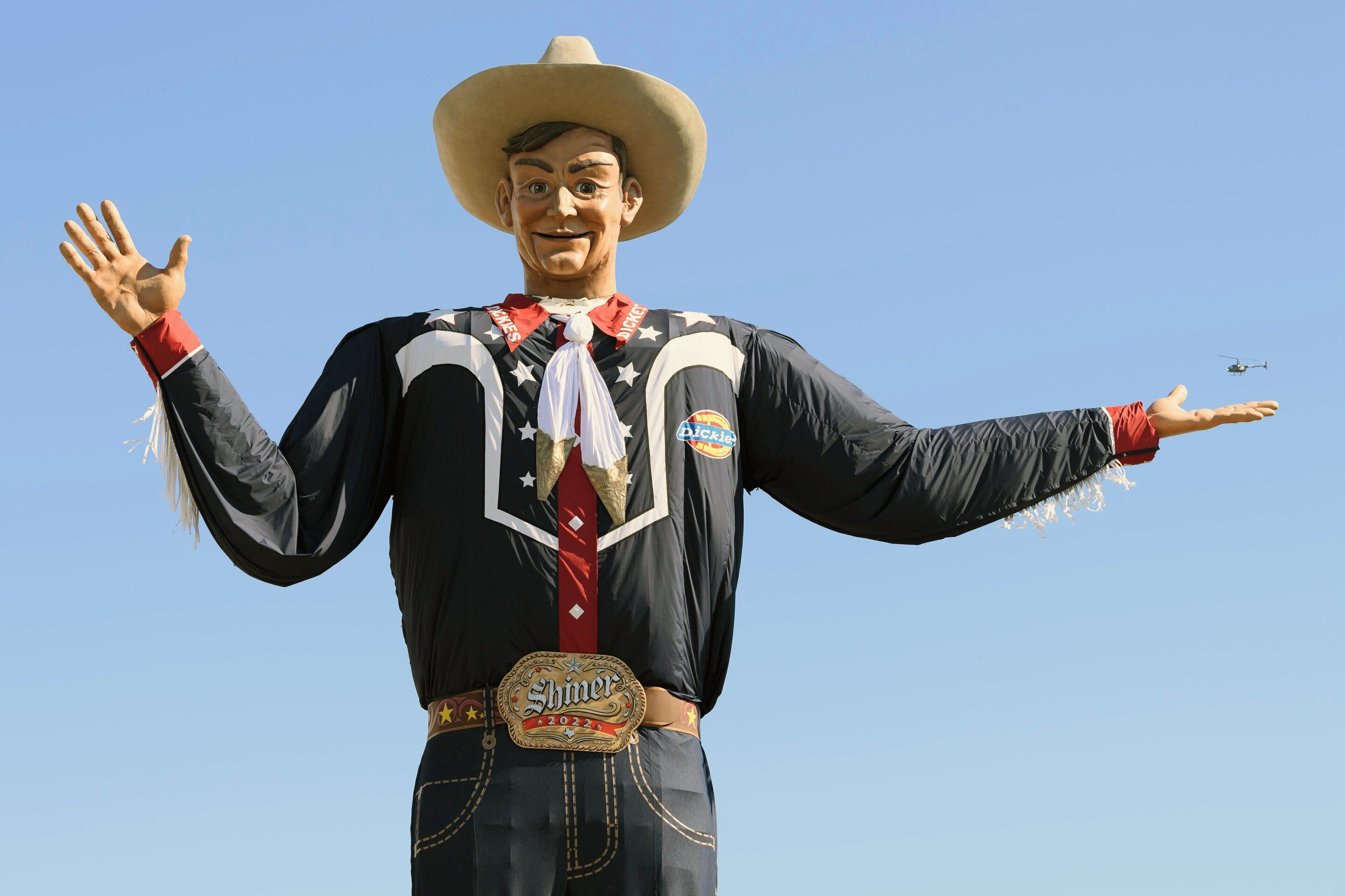 Une statue représentant une personne portant une chemise noire ornée d’un motif en étoile rouge et blanche, un grand chapeau et une ceinture avec une médaille.