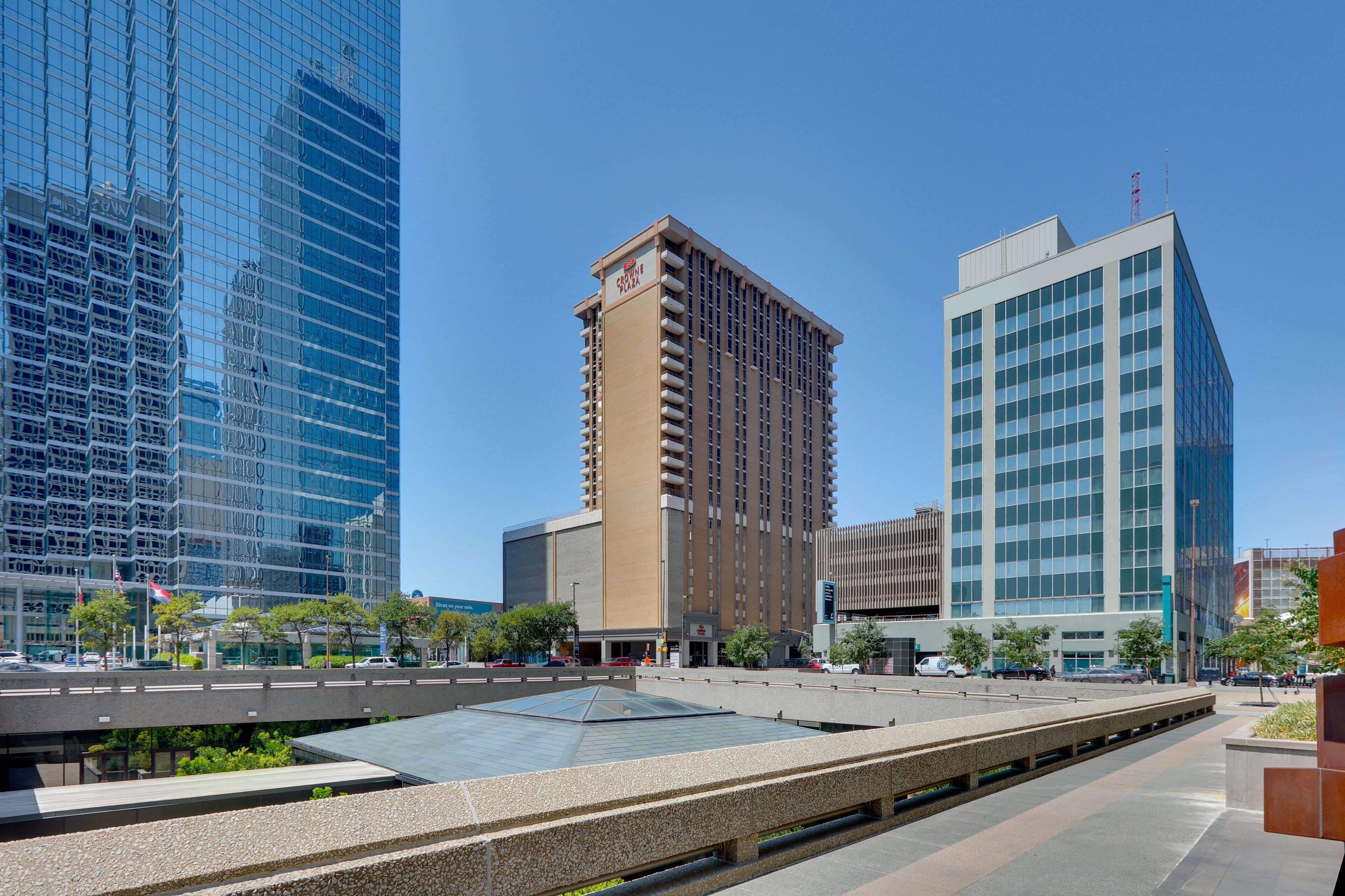 Una plaza urbana moderna con un atrio de cristal, rodeada de rascacielos.