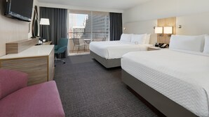 A hotel room with two beds, a desk, a TV, a chair, and a balcony with a city view. - Crowne Plaza Dallas Downtown by IHG (Dallas)
