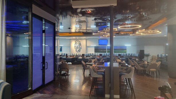 A modern restaurant with a bar area, seating arrangements, and a large screen. - Crowne Plaza Dallas Downtown by IHG (Dallas)