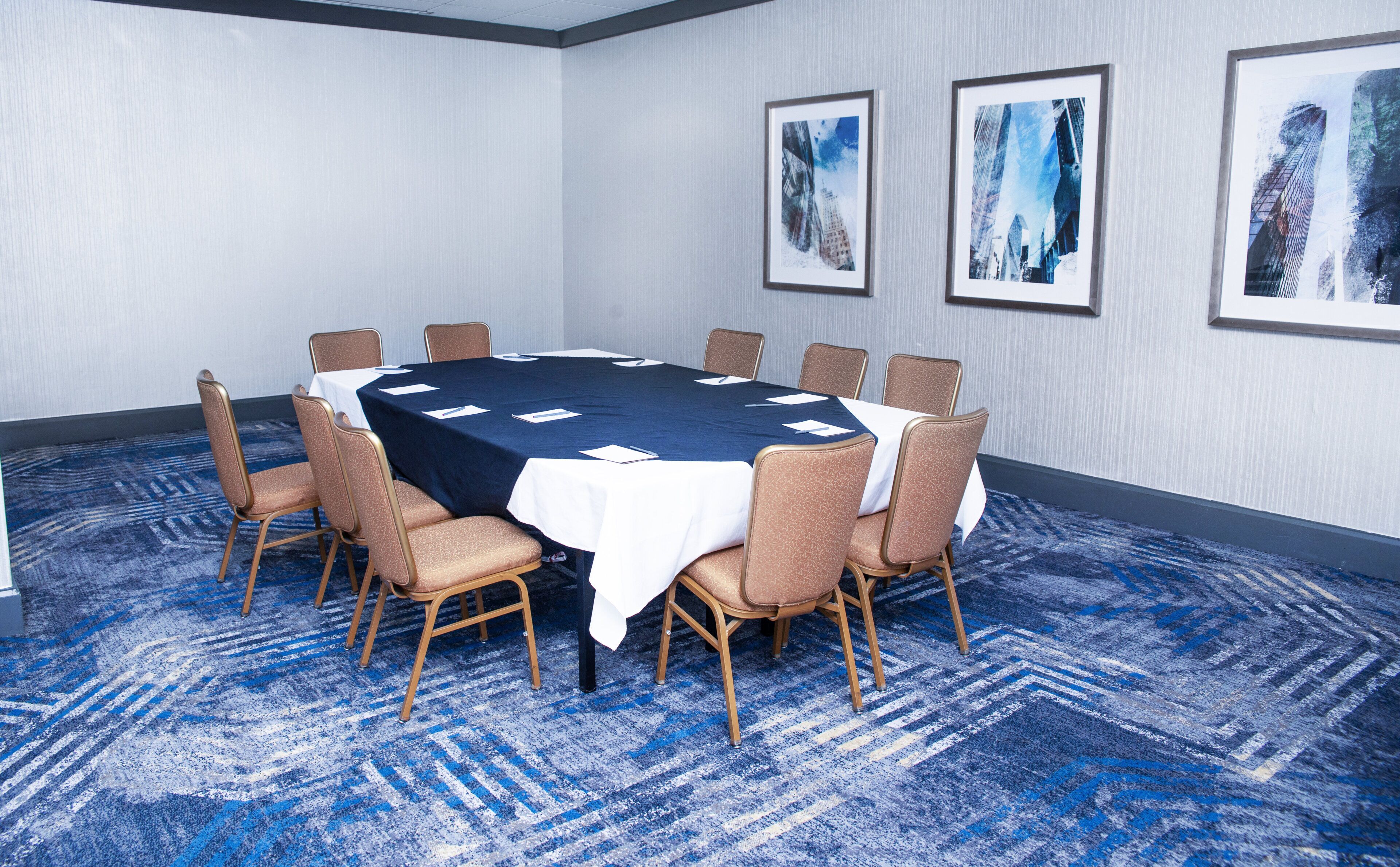 A conference room with a round table, chairs, and framed artwork on the walls.