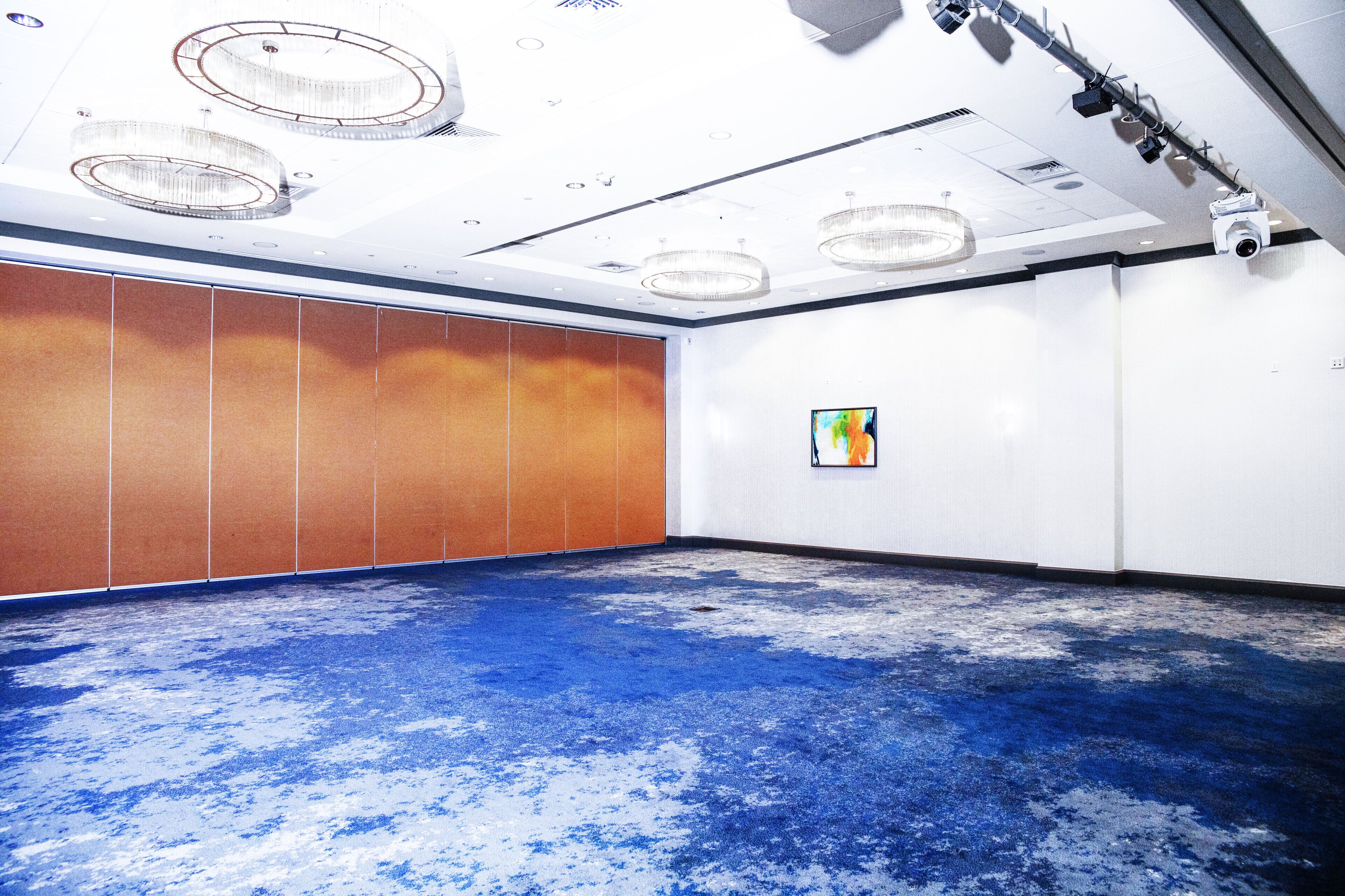 Una sala de conferencias con alfombra azul, paredes blancas y un ventanal grande.
