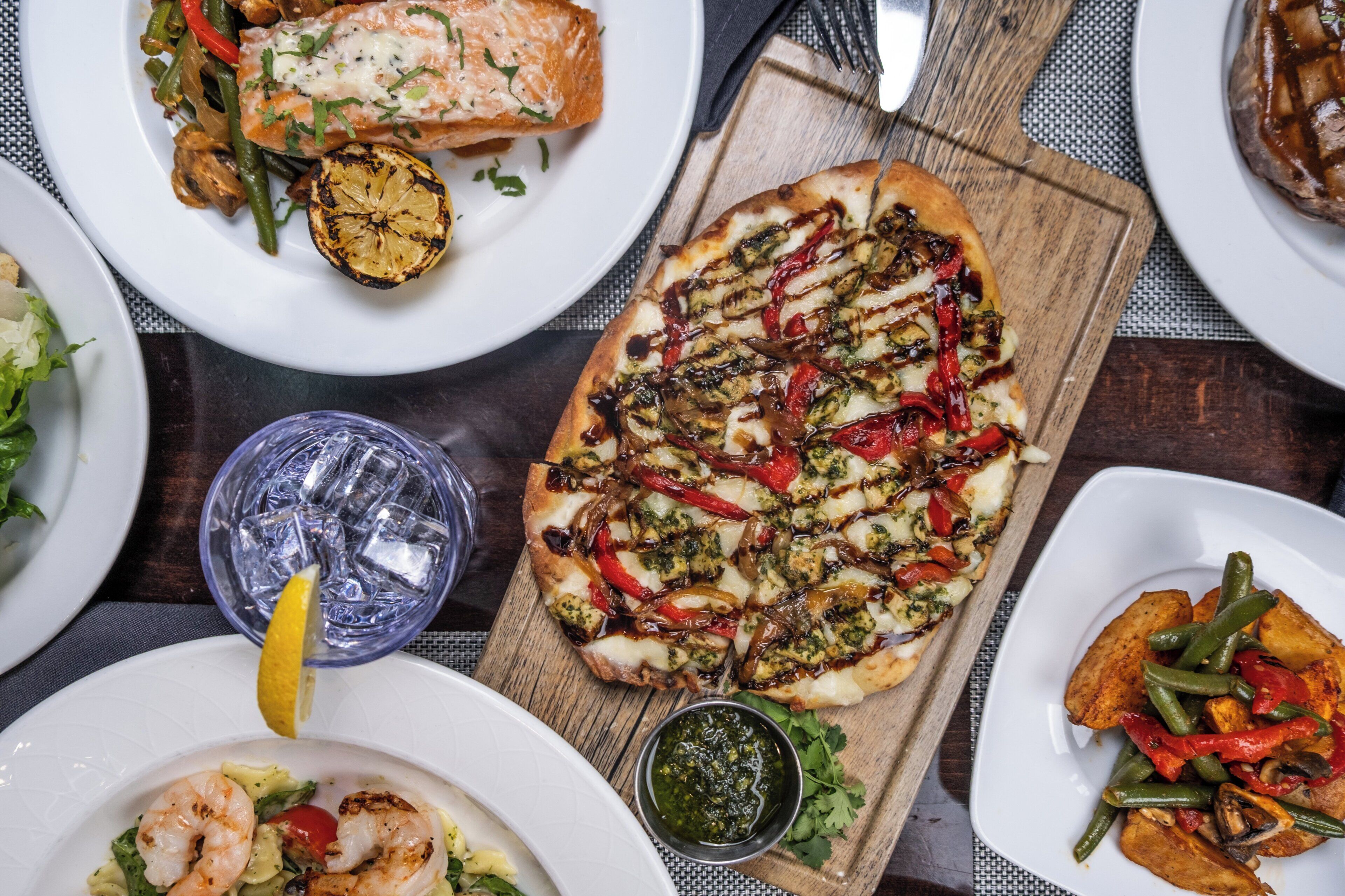 Ett urval av rätter, inklusive grillad lax, en pizza med grönsaker och en sallad, vilket antyder att det är en måltidsmiljö.