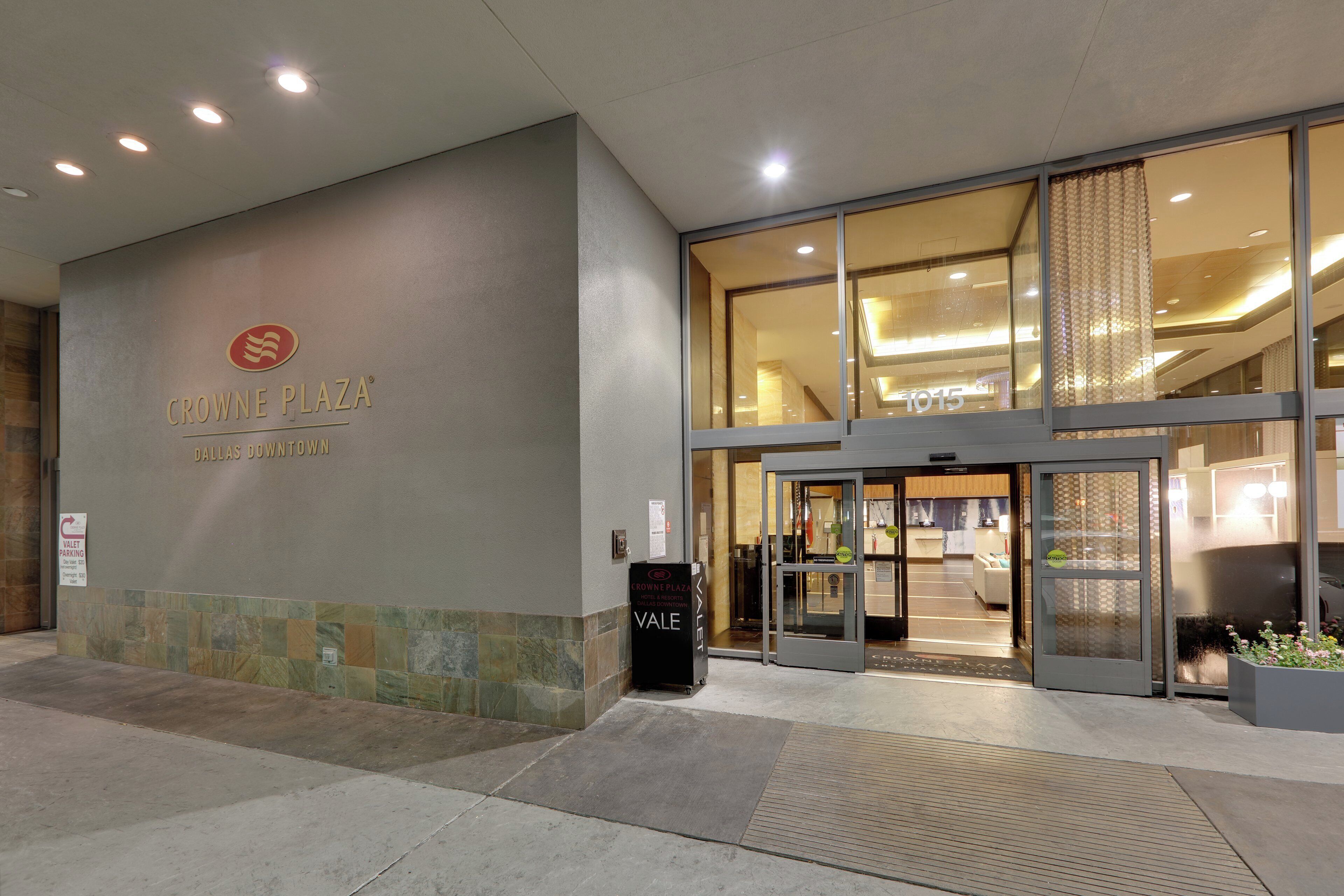 The exterior of Crowne Plaza Dallas Downtown with a modern entrance, valet parking sign, and a clear view into the lobby area.