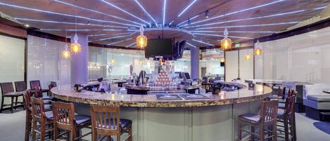 A bar area with a curved counter, multiple seating options, and a ceiling with linear lighting.