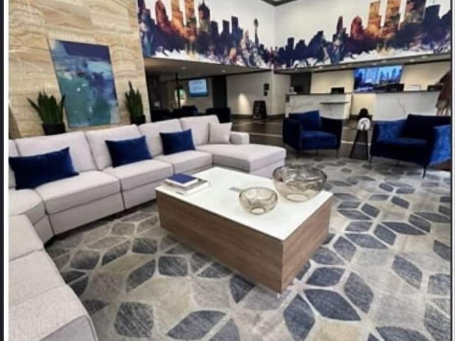 A modern lobby with a white sectional sofa, a wooden coffee table, and a patterned carpet.