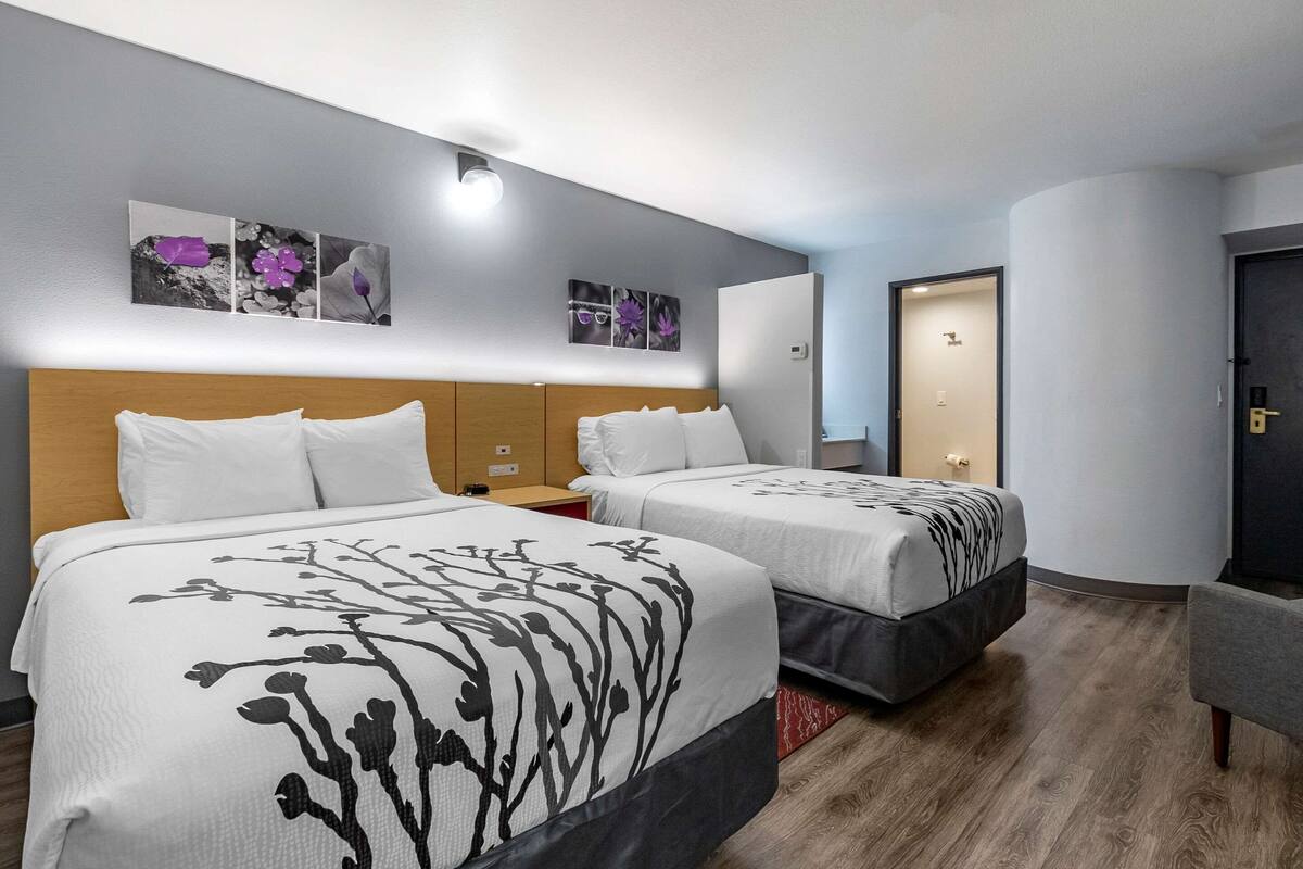 A hotel room with two beds, a wooden headboard, a nightstand, and a red rug.