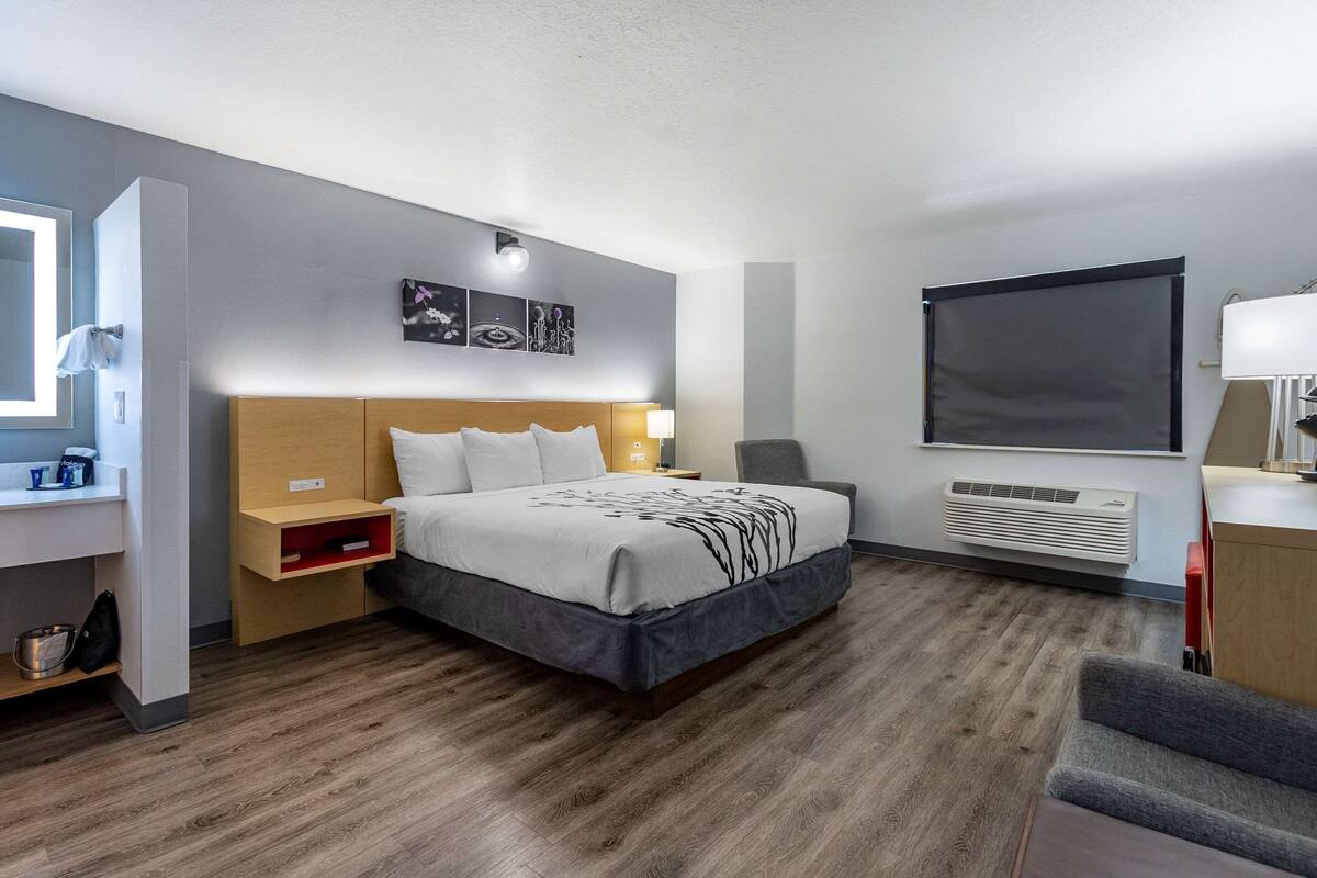 A modern hotel room with a large bed, a bedside table, a chair, a desk, and a window.
