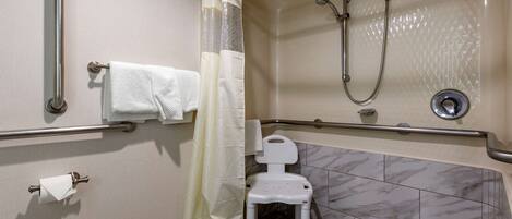 Une salle de bain équipée d’une douche, de barres d’appui, de toilettes et d’une chaise.