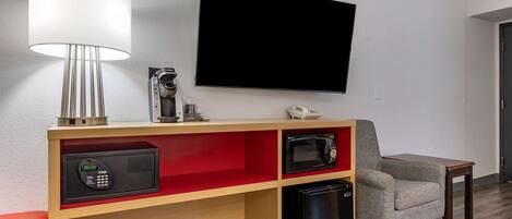 Habitación de hotel con televisión montada en la pared, microondas, mini refrigerador, cafetera y una silla.
