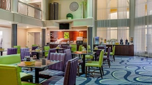 A hotel lobby with multiple seating areas, a central bar, and a staircase leading to an upper level.