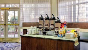 A coffee station with multiple coffee dispensers, a basket of bread, and various breakfast items.