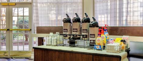 A coffee station with multiple coffee dispensers, a basket of bread, and various breakfast items.