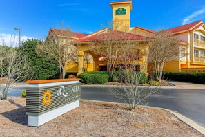 La Quinta by Wyndham features a distinctive yellow facade and red-tiled roof, with a central entrance flanked by two wings.