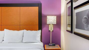 A hotel room with a wooden headboard, a white bed, a nightstand with a lamp, and framed artwork on the wall.