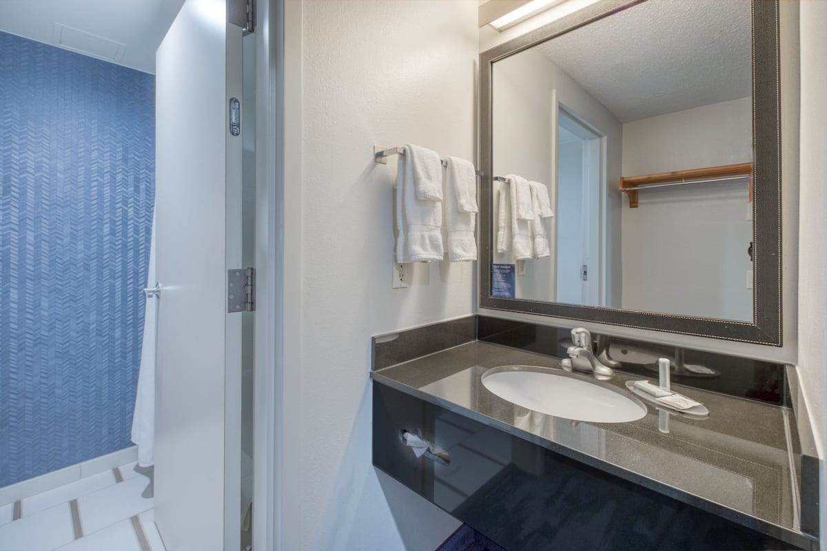 A bathroom with a glass shower enclosure, a white sink, and a mirror with a wooden frame.