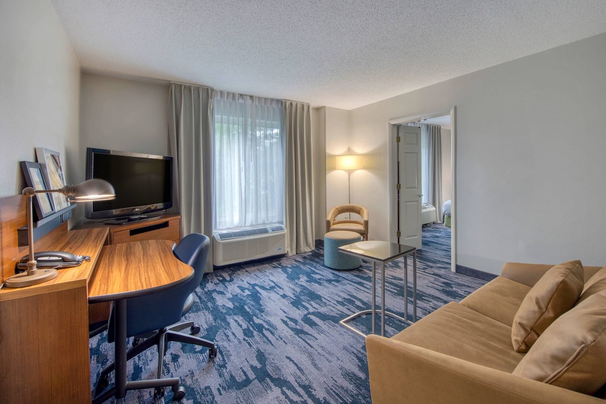 A hotel room with a wooden desk, a television, a sofa, a chair, and a lamp.