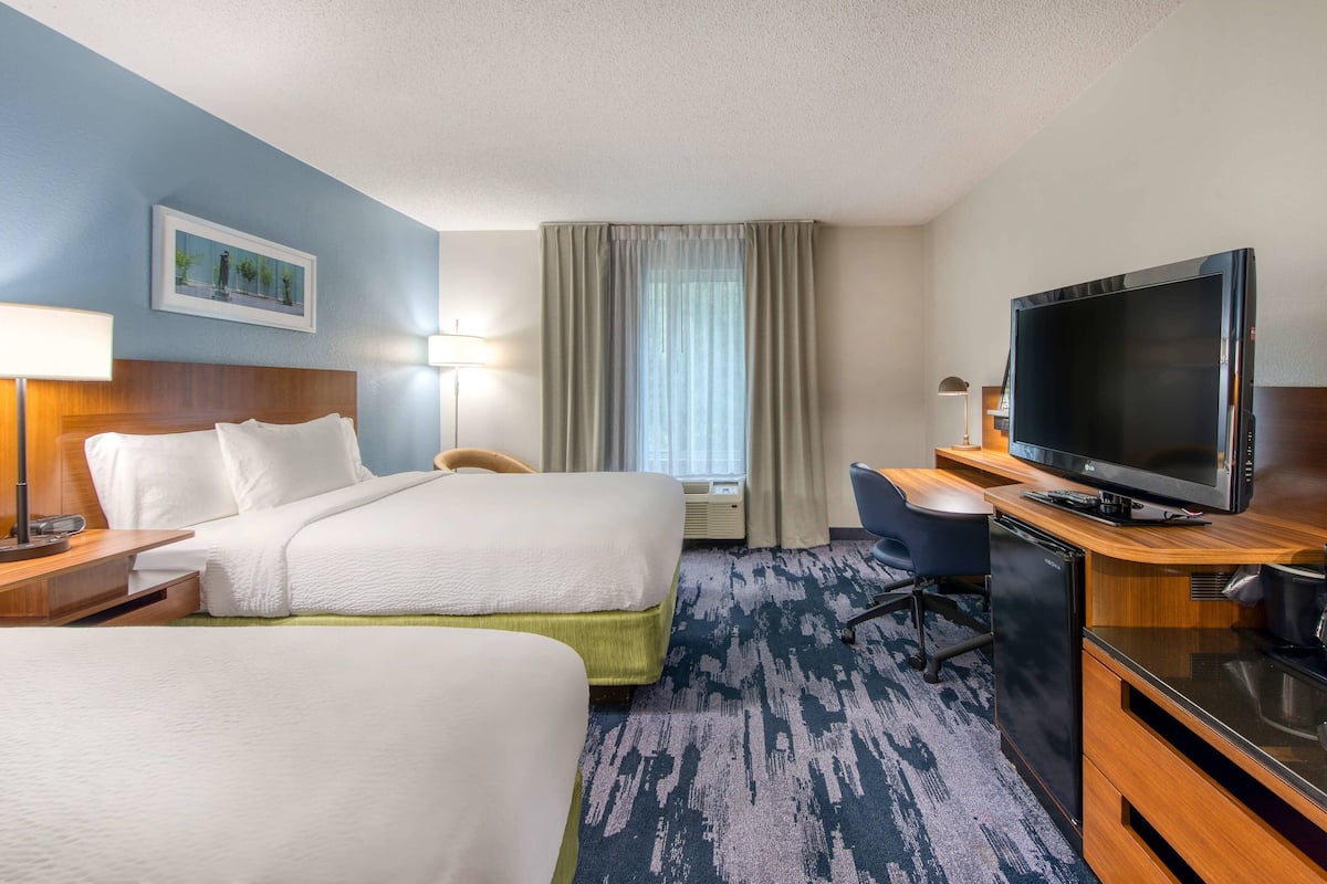 A hotel room with two beds, a desk with a television, a chair, and a window with curtains.