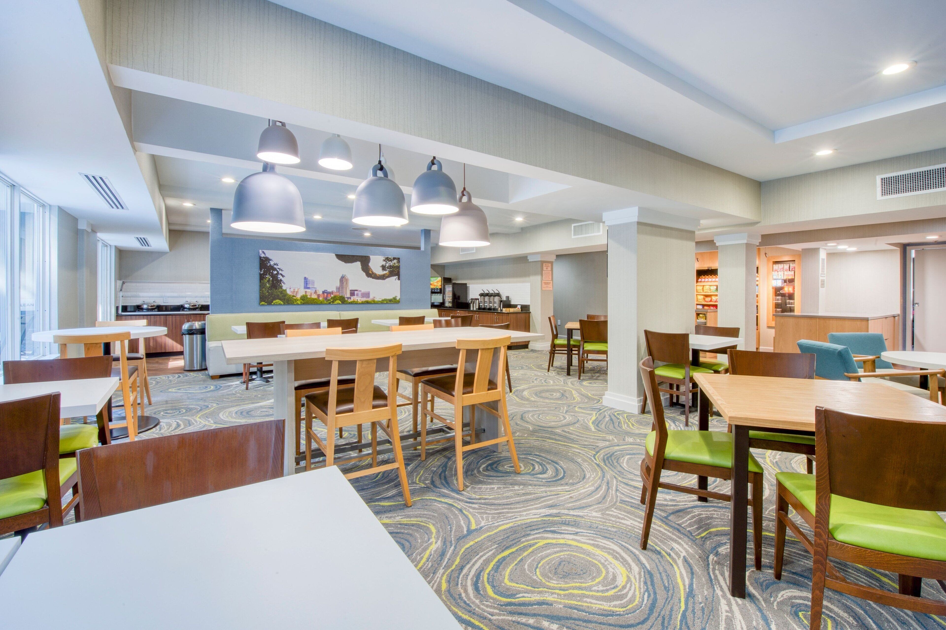 Un espace de restauration moderne, doté de plusieurs tables et chaises, d’un tapis à motifs et de luminaires suspendus.