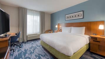 Habitación de hotel con una cama grande, un escritorio con computadora, un televisor y una ventana con cortinas.