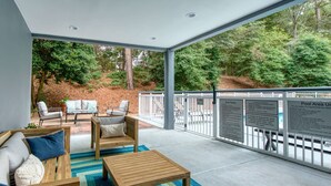 A covered outdoor seating area with a wooden table and chairs, a sofa with cushions, and a view of a wooded area. - Fairfield Inn By Marriott Raleigh Crabtree (Raleigh)