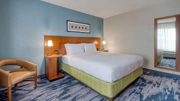 A hotel room with a bed, a chair, a nightstand, and a wall-mounted picture.