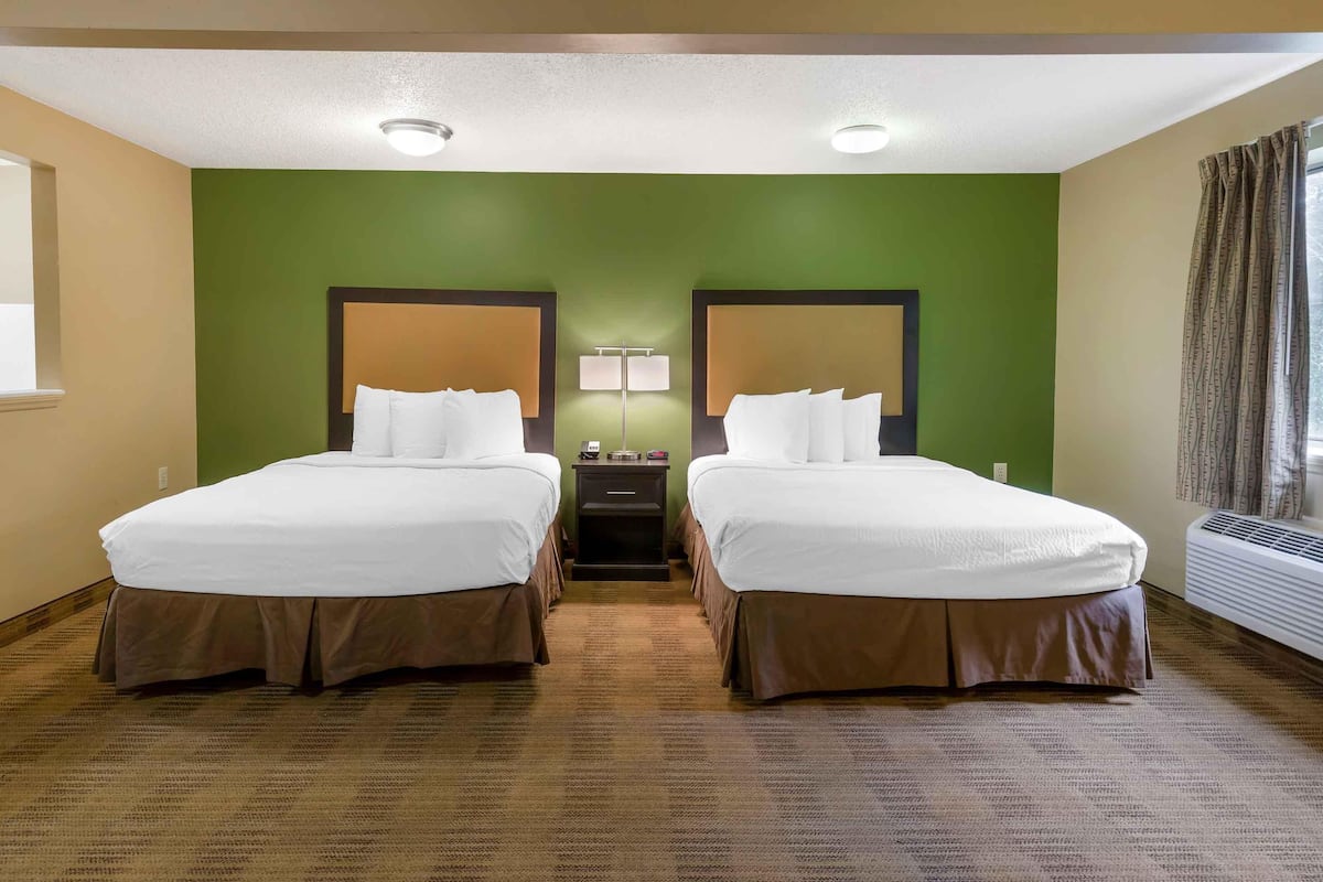 Ein Hotelzimmer mit zwei Betten, einem Nachttisch, einer Lampe und einem Fenster mit Vorhängen.