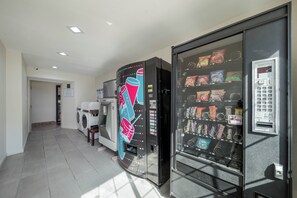 Een automaat met snacks en een machine op muntstukken, een wasmachine en een droger in een gang.